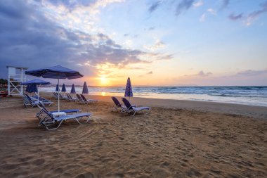 İnanılmaz bir gün doğumu. Şemsiyeli ve şezlonglu boş bir sahil. Güzel yaz manzaralı deniz manzarası. Sabah manzarası. Köpüklü yüksek dalgalar. Yunanistan 'ın Girit adasında romantik rahatlama.