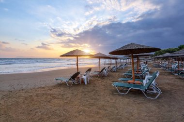 Saman şemsiyeli ve şezlonglu boş bir sahil. İnanılmaz bir gün doğumu. Güzel yaz manzaralı deniz manzarası. 2020 yaz karantina seyahati. Yunanistan Girit adasında rahatla.