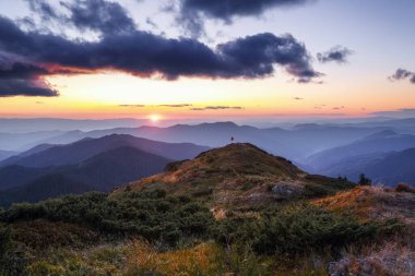Güzel gün batımı. Dağların manzarası. Yabanmersinli çalıların arasındaki çimenlikte kız spor kıyafetleri ve turistik çadırlarda sırt çantasıyla kalıyor. Kişi silueti.