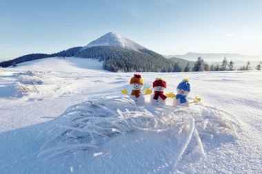 Karlı çimlerde şapkalı ve eşarplı küçük kardan adamlar. Güzel kış günbatımı arka planı. Yüksek dağlı manzara. Mutlu Noeller ve mutlu yıllar..