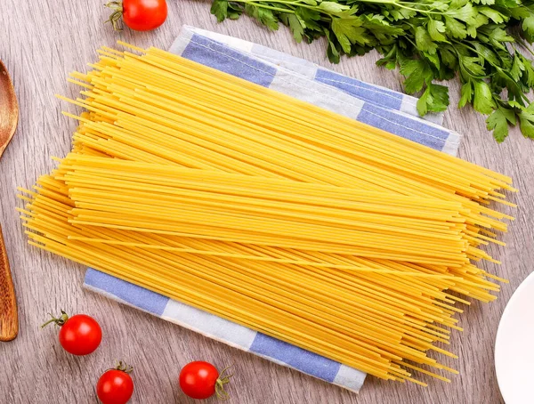 Çiğ spagetti makarnası, domates ve ahşap arka planda yakın plan yeşillikler. Üst görünüm