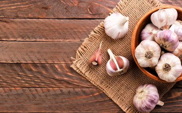 Bir tabak dolusu sarımsak ve ahşap arka planda bir diş sarımsak. Boşluğu kopyala