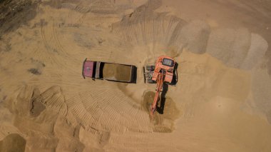 Aerial view of excavator pours sand into the truck. On the construction site top view. Shooting from the drone/