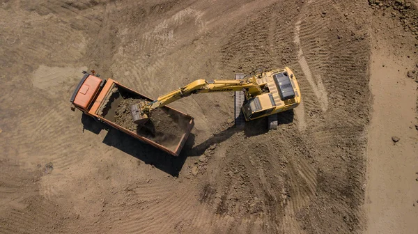 Aerial view of excavator pours sand into the truck. On the construction site top view. Shooting from the drone/
