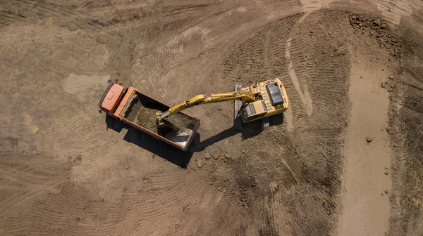 Aerial view of excavator pours sand into the truck. On the construction site top view. Shooting from the drone/