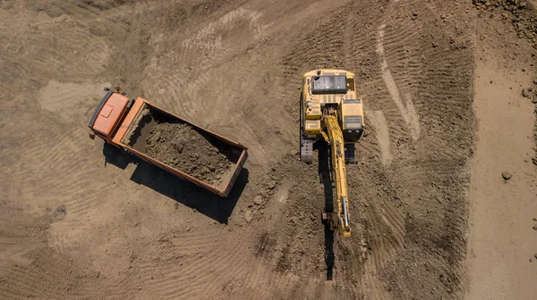 Aerial view of excavator pours sand into the truck. On the construction site top view. Shooting from the drone/