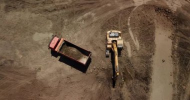 Aerial view of excavator pours sand into the truck. On the construction site top view. Shooting from the drone/