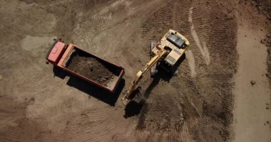 Aerial view of excavator pours sand into the truck. On the construction site top view. Shooting from the drone/