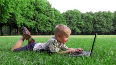 6 yaşındaki çocuk laptop, yüzü neşeli duygular bir çim üzerinde bırakır