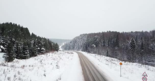 Flygfoto flyga över motorvägen vintern vägen bland snöiga skogen. — Stockvideo