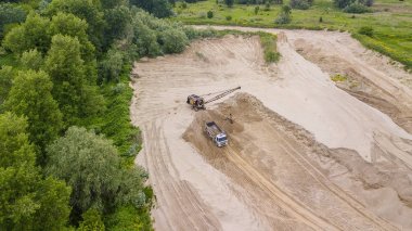 Ekskavatörün manzarasını aşağı yaslamak kamyonun içine kum döküyor, ağaçların yanında. Şantiyede.