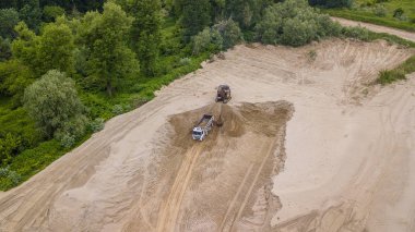 Ekskavatörün manzarasını aşağı yaslamak kamyonun içine kum döküyor, ağaçların yanında. Şantiyede.