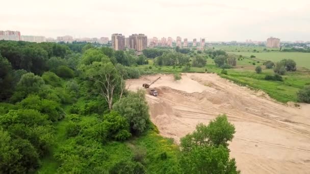 Vista de arriba hacia abajo de la excavadora vierte arena en el camión, cerca de los árboles y el edificio de la ciudad . — Vídeos de Stock