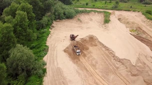 Widok z góry na dół koparki wylewa piasek do ciężarówki, w pobliżu drzew. Na budowie. — Wideo stockowe