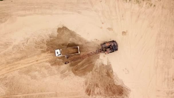 Вид сверху на экскаватор засыпает песок в грузовик, рядом с деревьями. На строительной площадке . — стоковое видео
