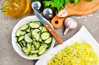 Vejetaryen salata, kıyılmış lahana ve mutfak masasında maydanoz ve sarımsak ile dilimlenmiş salatalık için malzemeler