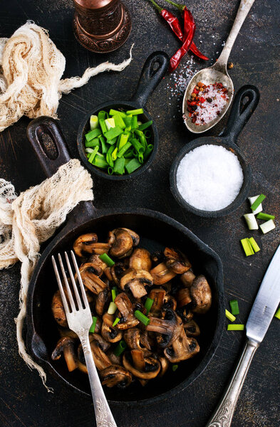 Fried mushrooms and green onion in the frying pan, top view