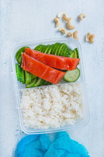 top view of salmon fish with boiled rice and cucumber in lunch box