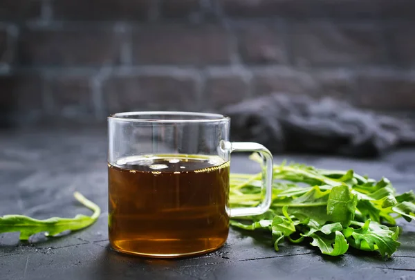 Fresh green arugula leaves and oil in glass cup on grey tabletop