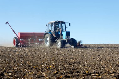 Kırmızı bir mibzer ile mavi traktör parlak güneşli sonbahar günü alanında çalışır