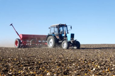 Kırmızı bir mibzer ile mavi traktör parlak güneşli sonbahar günü alanında çalışır
