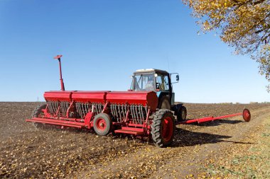 Kırmızı bir mibzer ile mavi traktör parlak güneşli sonbahar günü alanında çalışır