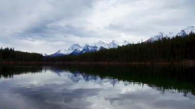 Bir bulutlu gün kar dağ ve orman Banff Ulusal Parkı'nda gölde Herbert.