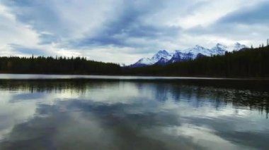 Herbert Gölü timelapse kar dağ ve orman yansıması ile bulutlu bir günde Banff Ulusal Parkı'nda panoramik görünümü kaydırma.