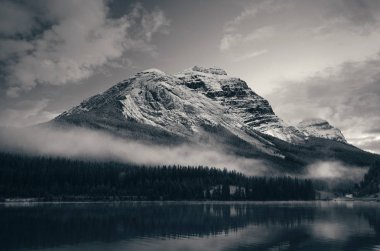 Kanada Banff Ulusal Parkı 'ndaki sisli bir alacakaranlıkta gölün yansımasıyla karla kaplı dağ..