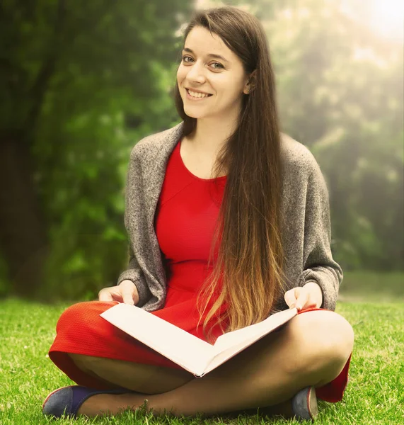 Beautiful woman reading book in nature. Young attractive student in red dress studying and reading a book. (Relax, rest, education concept,  recreation).