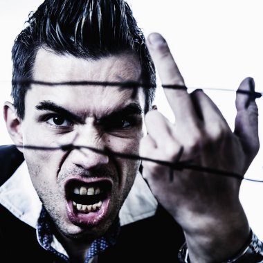 Fuck the system concept. Man behind a barbed wire shows a middle finger gesture as symbol of pain and lack of freedom.