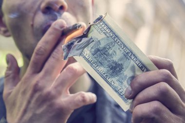 Servet ve başarının sembolü olarak 100 dolarlık banknotla puro yakan genç vahşi adam.