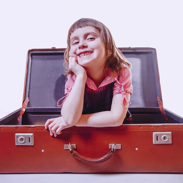 I am happy to travel, I am ready for the trip! Happy cute little child girl sitting on vintage suitcase.