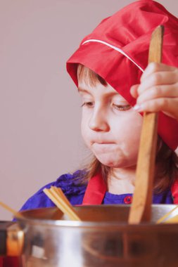 Küçük tatlı kız şefe yakın yemek pişiriyor, ortalığı karıştırıyor.