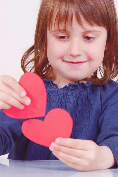 Humorná fotka roztomilé holčičky hrající si s červenými srdci — Stock fotografie