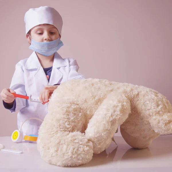 Küçük kız doktorculuk oynuyor ve oyuncak ayı enjekte ediyor. — Stok fotoğraf