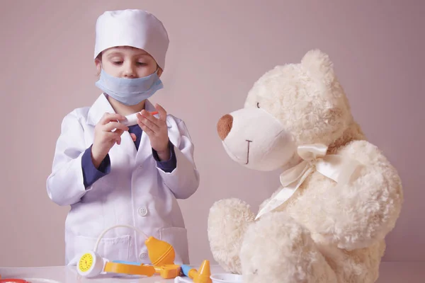 Küçük kız doktorculuk oynuyor ve oyuncak ayı enjekte ediyor. — Stok fotoğraf