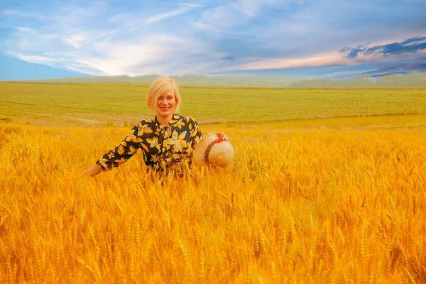劇的な空の背景に対して小麦畑に立って若い美しいブロンドの女性 夏休みのコンセプト — ストック写真