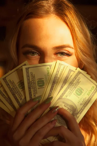 Money is best motivation. Close up portrait of young beautiful woman holding  US Dollar bills as symbol of wealth and success. Image with deep shadows.