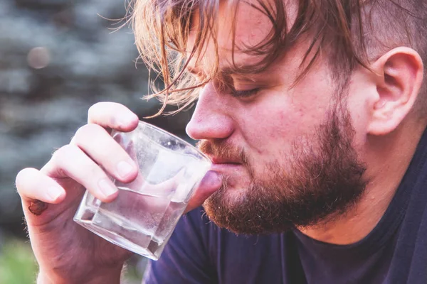 Drinking man. Close up unhappy sad man sitting outdoors and drinking vodka.