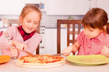 İki küçük bayan arkadaş pizzayı çatal ve bıçakla kestiler..