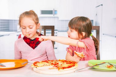 En iyi yiyeceklerin sembolü olarak pizza yiyen şirin küçük kızların komik bir görüntüsü. Yatay resim.