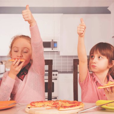 Pizzaya bayılırız! Tatlı küçük kızlar pizza yiyor ve OK jesti yapıyor. Parmaklar üzerine seçici odaklanma. 