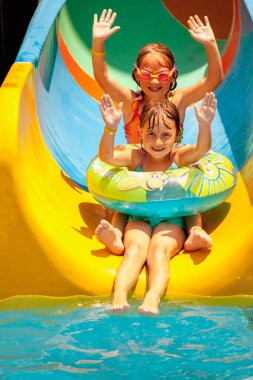 Yaz boyunca su kaydırağına giden iki tatlı genç kız. Yaz tatili, macera ve mutlu çocukluk kavramı. Dikey resim.