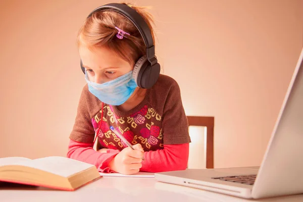 Distance learning online education. Portrait of young cute schoolgirl in headphones studies at home and does school homework.