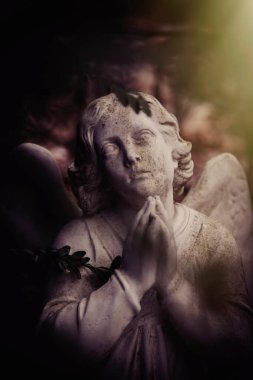 Mavi gökyüzünde dua eden bir melek figürü. Güneş ışınlarında antik taş heykel