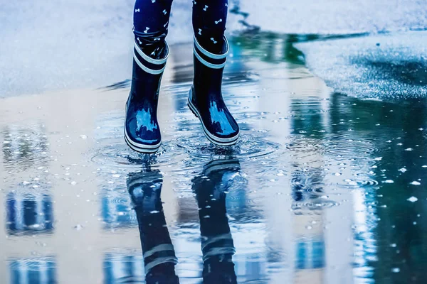 Feet of child in rubber boots jumping over a puddle in the rain.