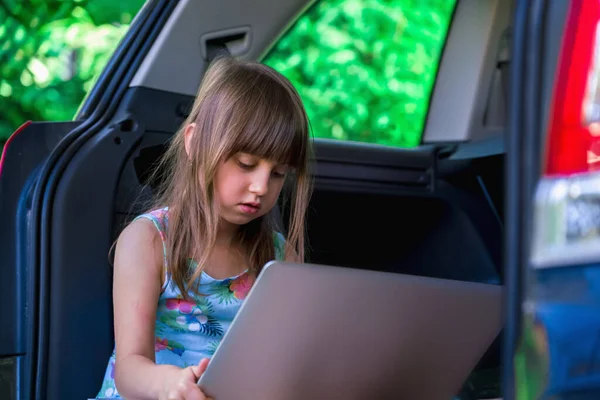 Learn always and everywhere. Young beautiful girl sitting in the car and using laptop. Horizontal image.
