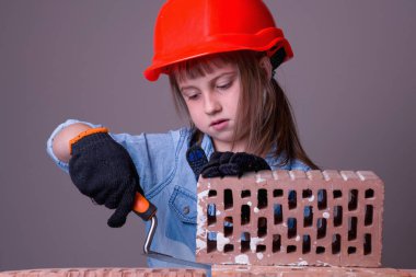 Şirin küçük kız müteahhidin komik görüntüsü tuğla duvar örüyor. İnşaat ve onarım hizmetleri kavramı. Yatay resim.