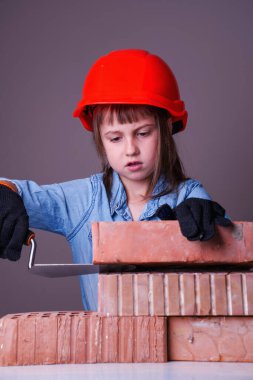 Şirin küçük kız müteahhidin komik görüntüsü tuğla duvar örüyor. Bina hizmetleri kavramı.